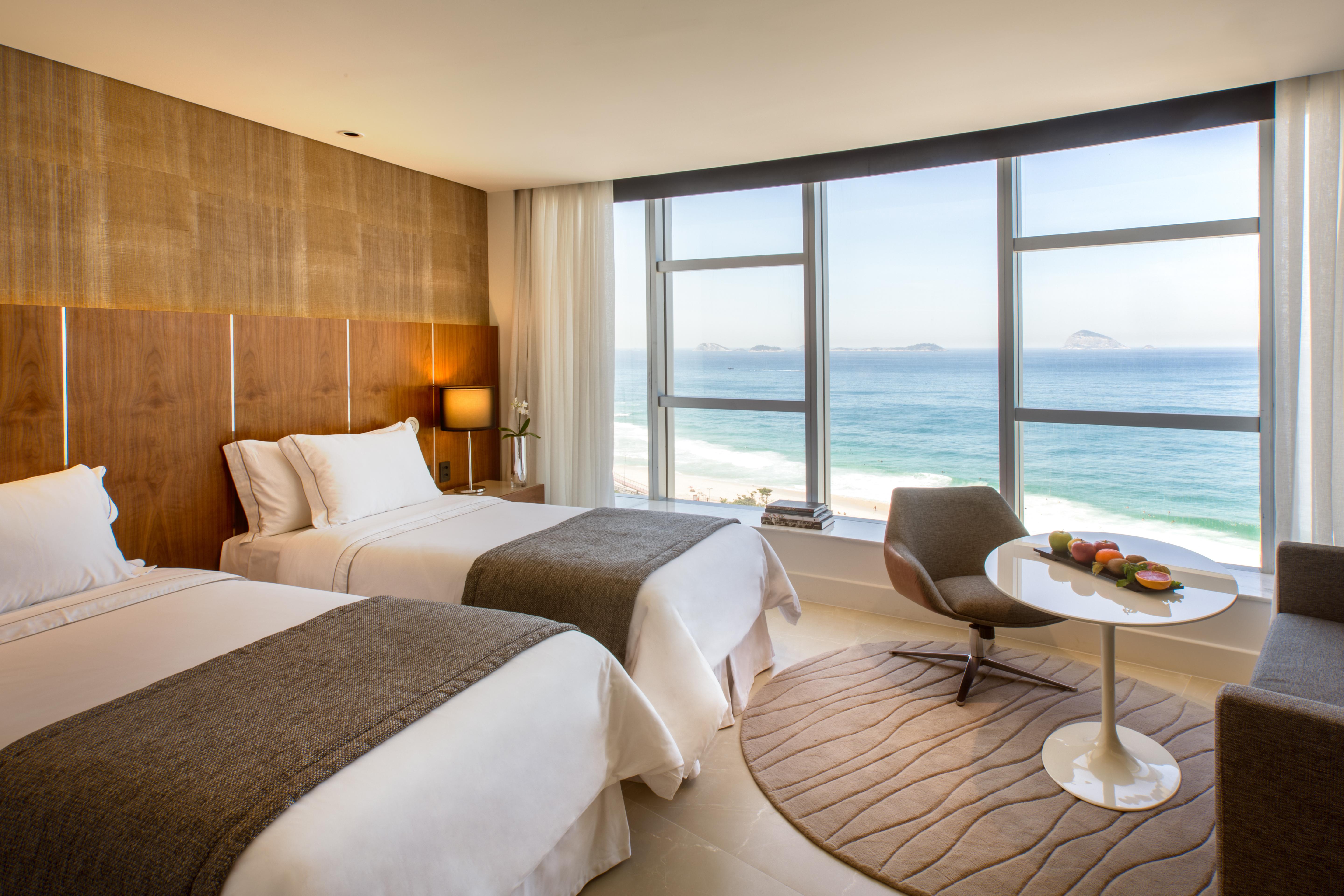 Hotel Nacional Rio De Janeiro - Oficial エクステリア 写真 The photo shows a modern hotel room with two beds adorned in white linens and gray throws. Large windows allow natural light to flood the space, offering a stunning view of the ocean. In the corner, there's a comfortable chair and a small round table